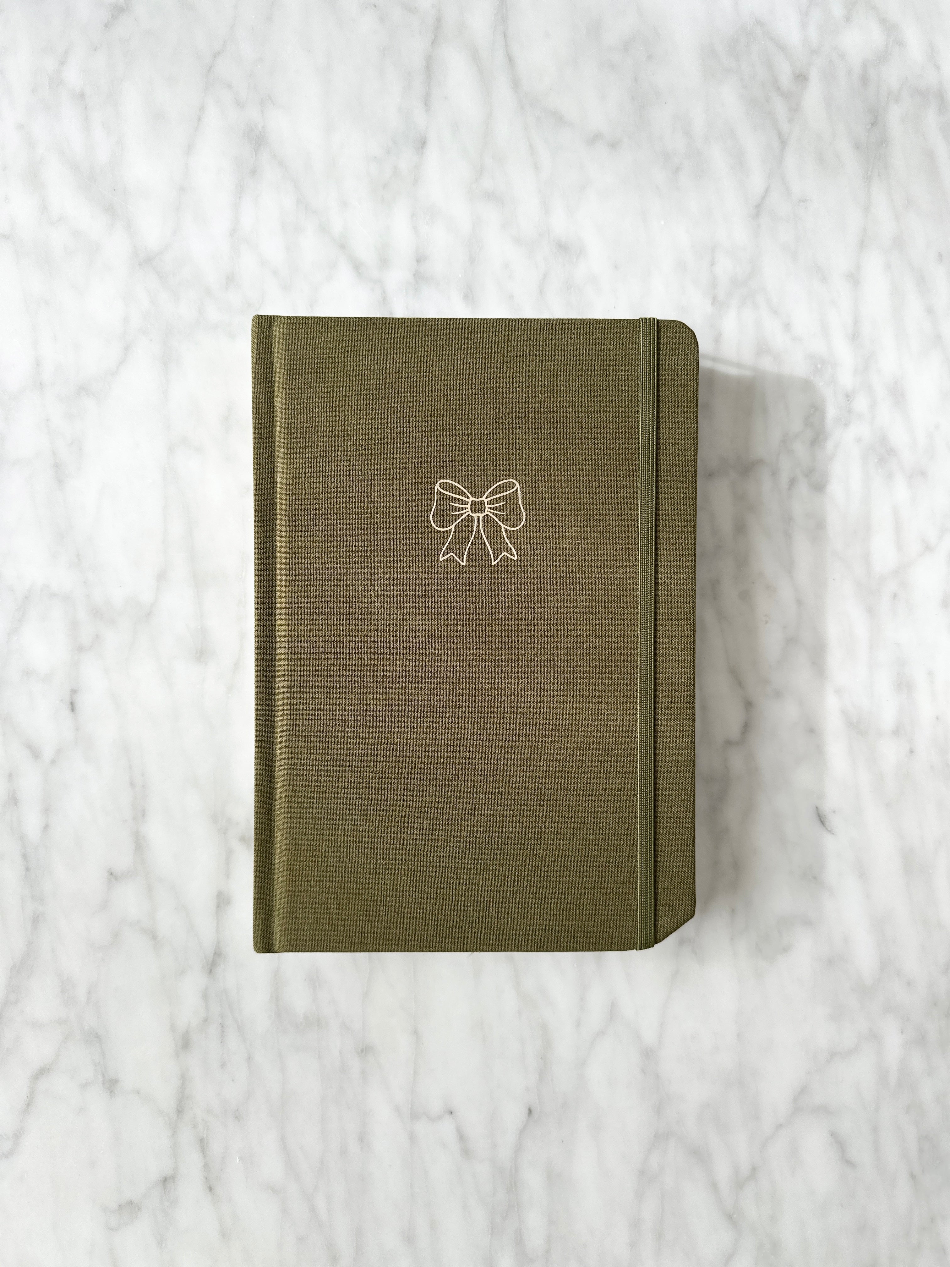 High quality linen bullet journal in olive green with a gold bow design on the front